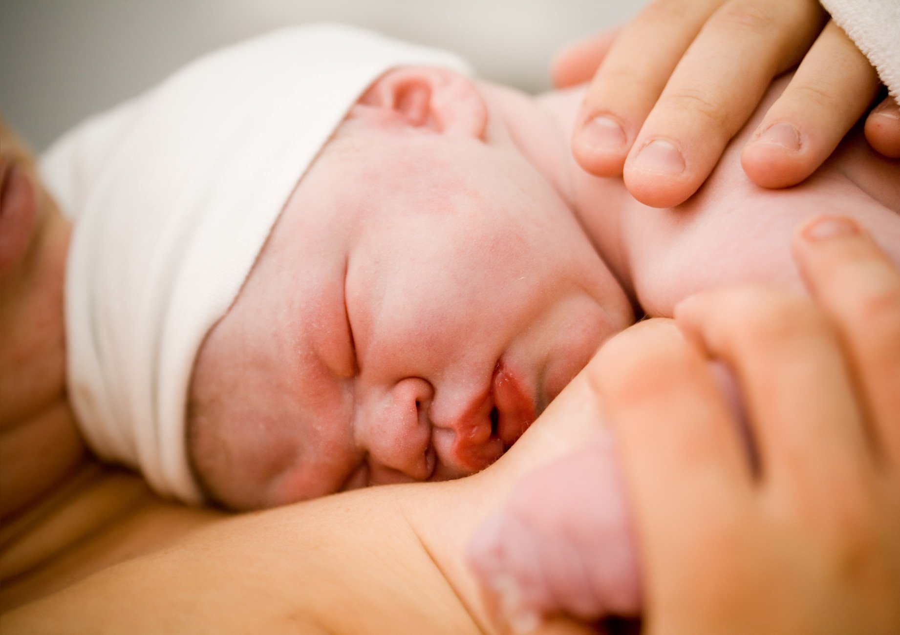 Frisch geborenes Baby mit weisser Kappe, für Bonding direkt auf die Brust der Mutter gelegt
